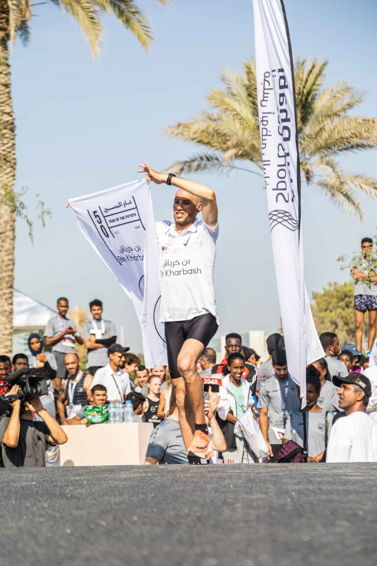 Runner running at Zayed Charity Marathon Abu Dhabi 2022 with a Year of the Fiftieth banner
